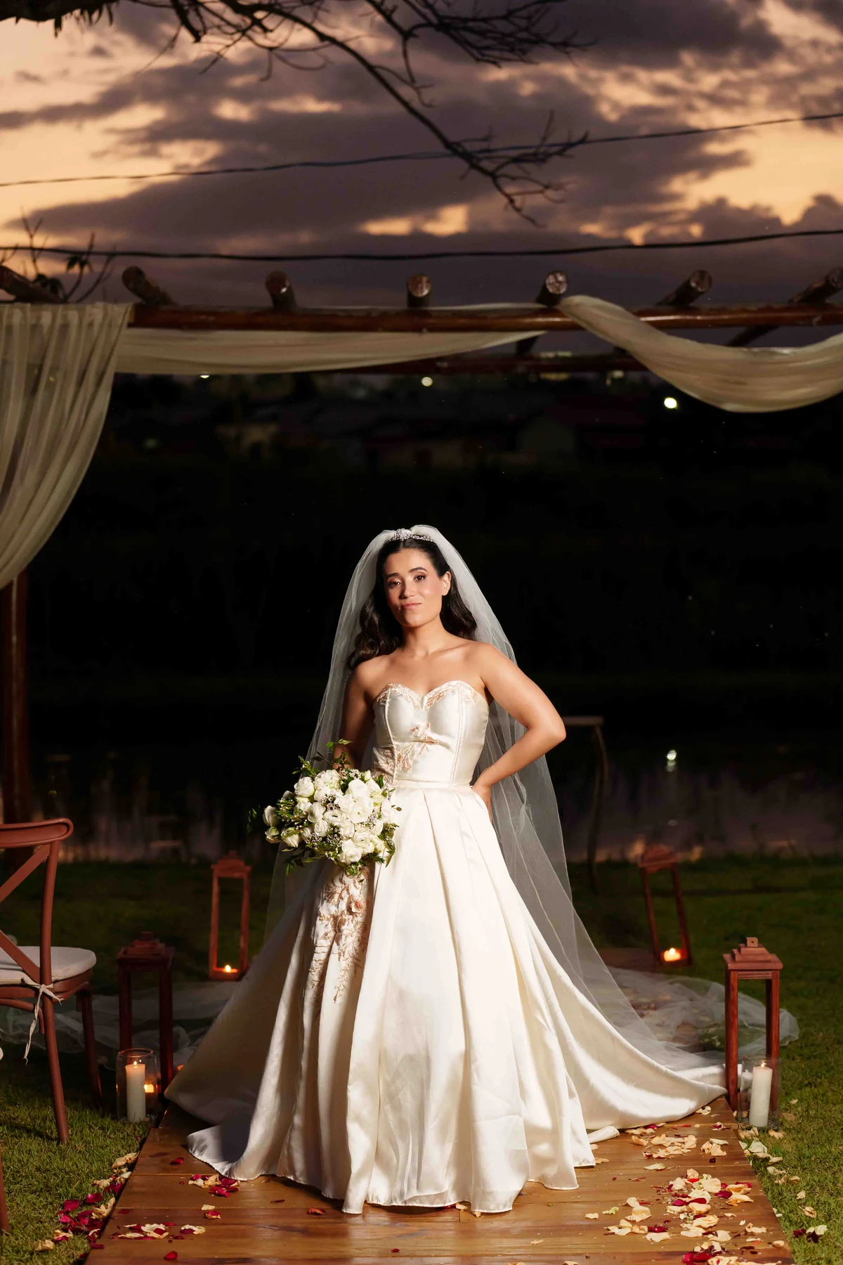 Gabi com seu vestido e buquê no jardim ao entardecer