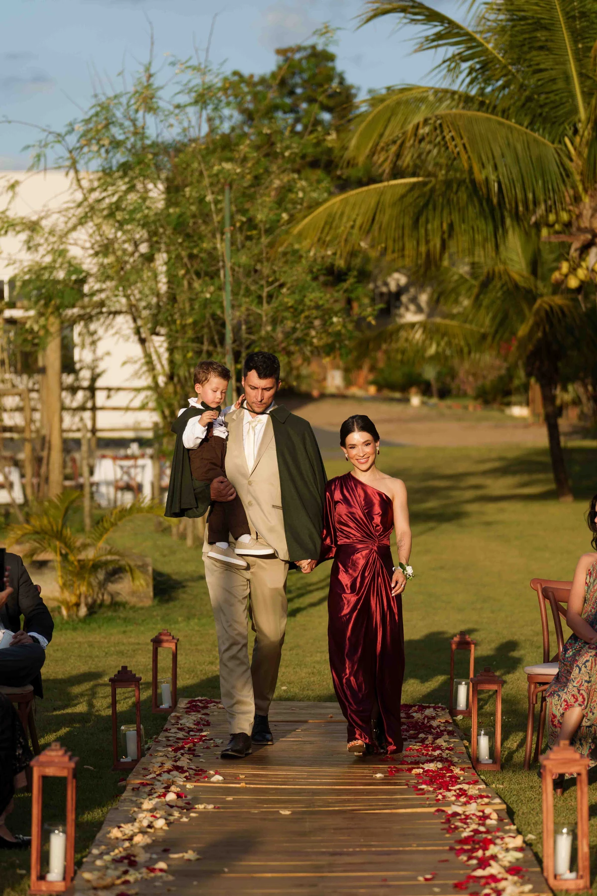 Entrada na cerimônia com vestido rubi, traje claro, madeira e pétalas em tons de vermelho e marfim