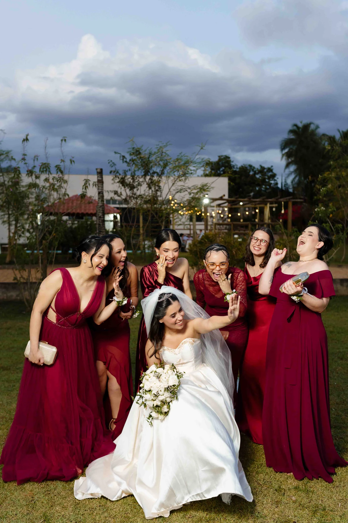 Gabi com as madrinhas sorrindo, com vestidos em diferentes tonalidades de vermelho profundo